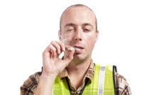 A young man in construction safety vest smokes a marijuana cigarette.
